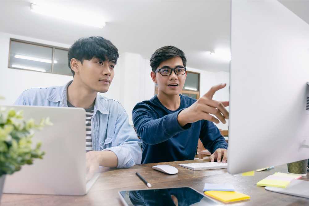 Two men at work are looking at a desktop together.