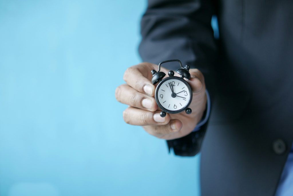 A Man in Suit Holding a Little Alarm Clock
