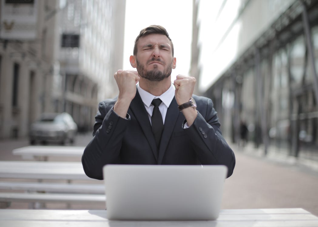 Businessman Sitting Outdoors in Front of a Laptop, Celebrating Success with Clenched Fists and a Triumphant Expression